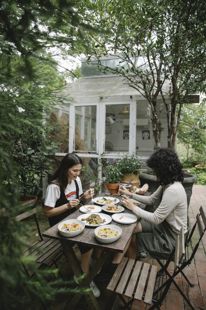 High angle of female farmers having lunch with different dishes in garden among green plants